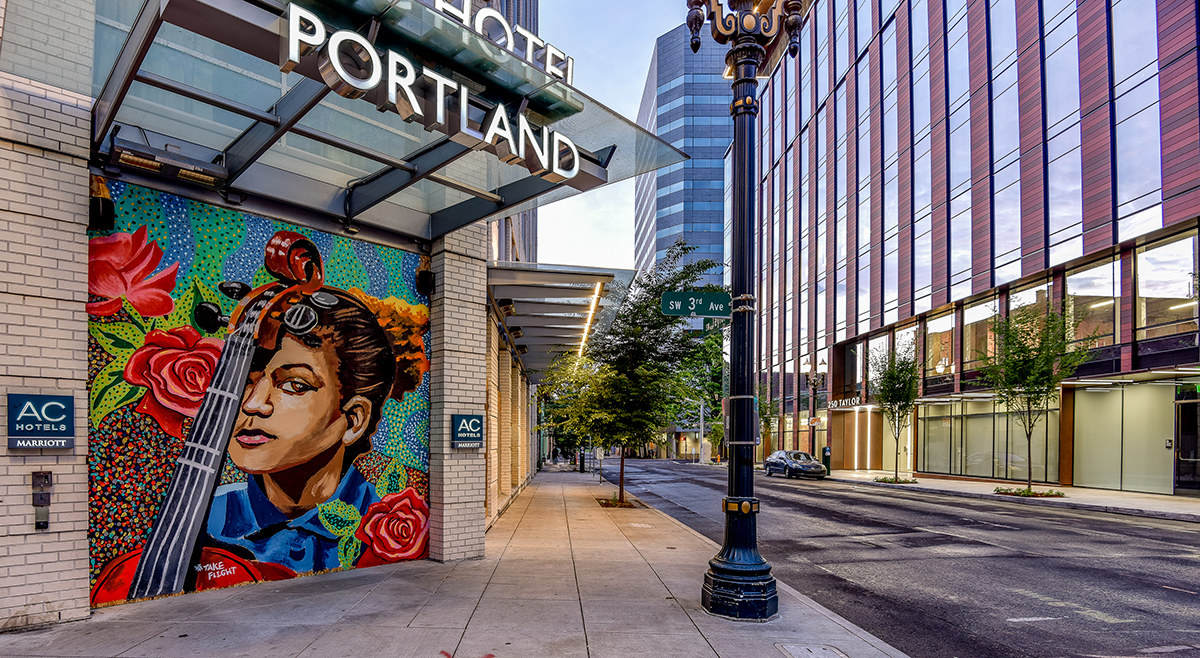 A mural outside the AC Hotel in Portland of a woman with a cello, accompanied by the hashtag #takeflight
