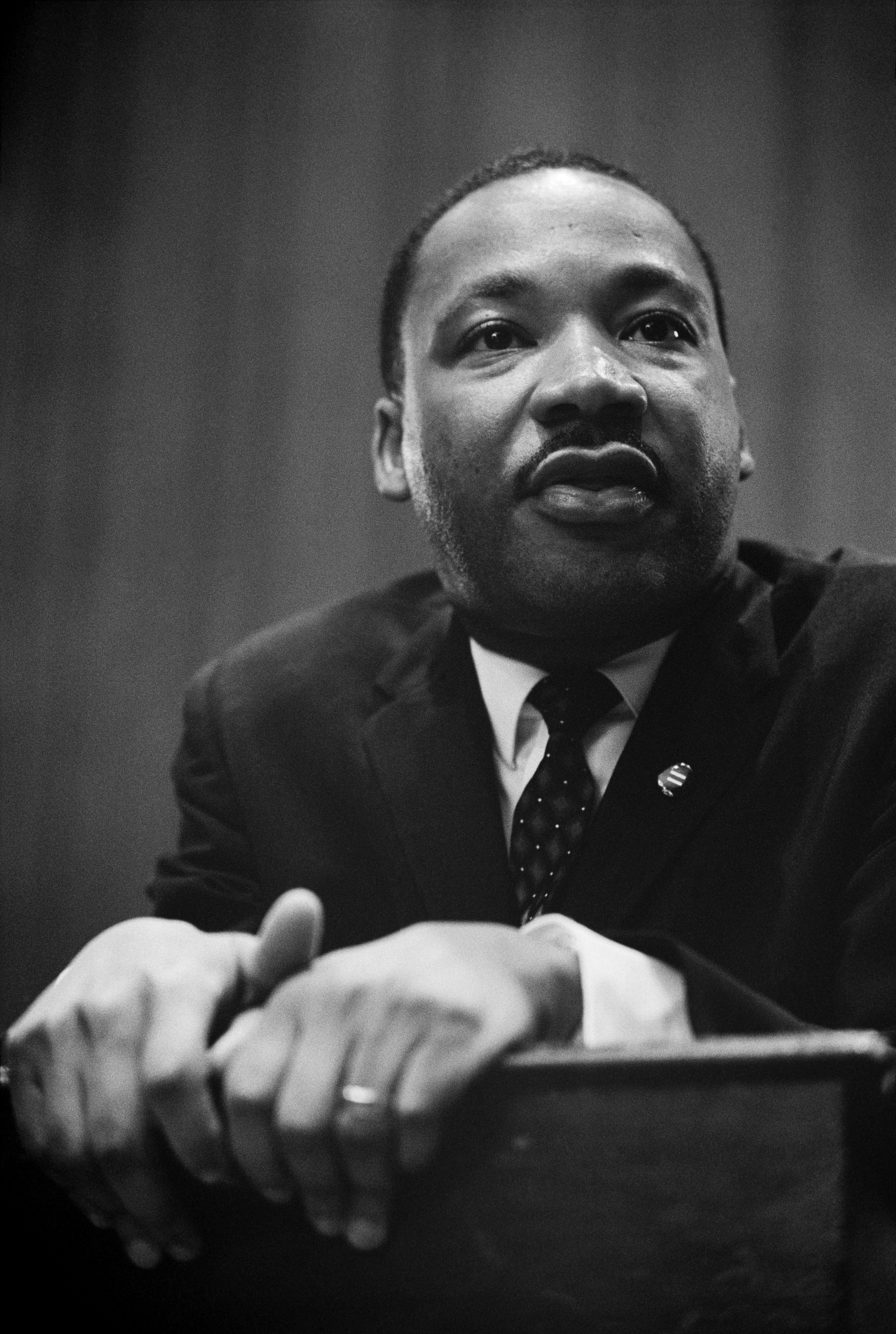 Rev. Dr. Martin Luther King leans over a podium in a black and white photo.
