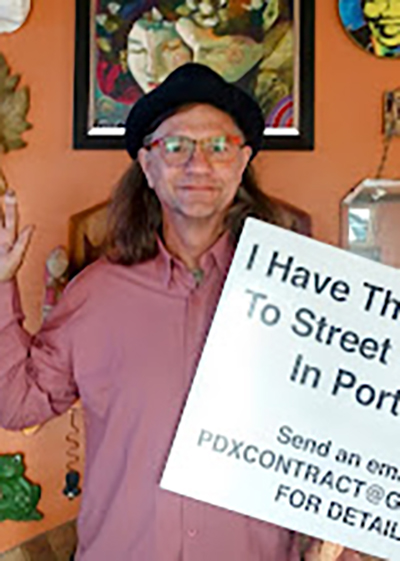 Dale Hardt poses for the photo with a fist raised and holding a sign that reads, "I have the solution to street camping in Portland."