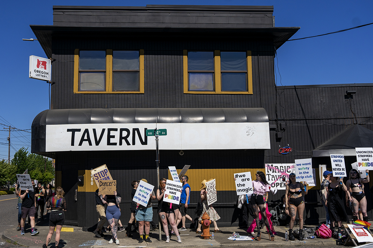 A group of people stands outside Magic Tavern holding signs.