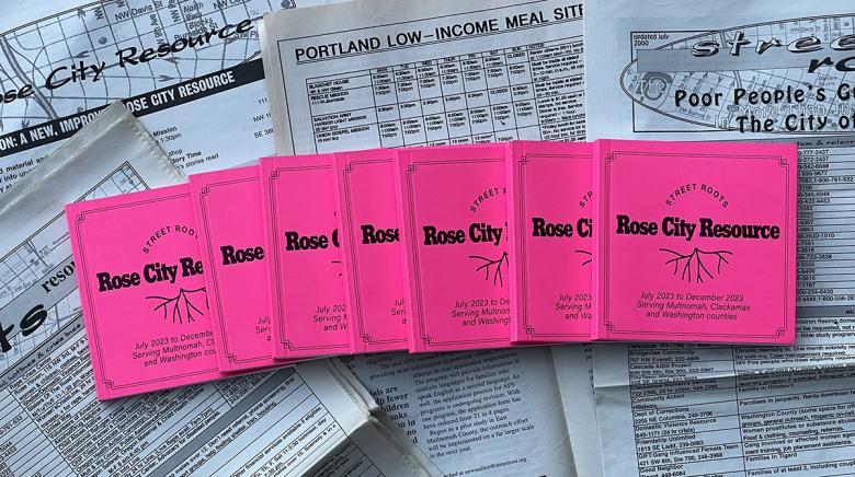 Seven copies of the July to December 2023 edition of the Resource Guide, colored neon pink, are spread in an arch overlaying each other on top of old copies of the Burnside Cadillac Newspaper, Street Roots' predecessor. 