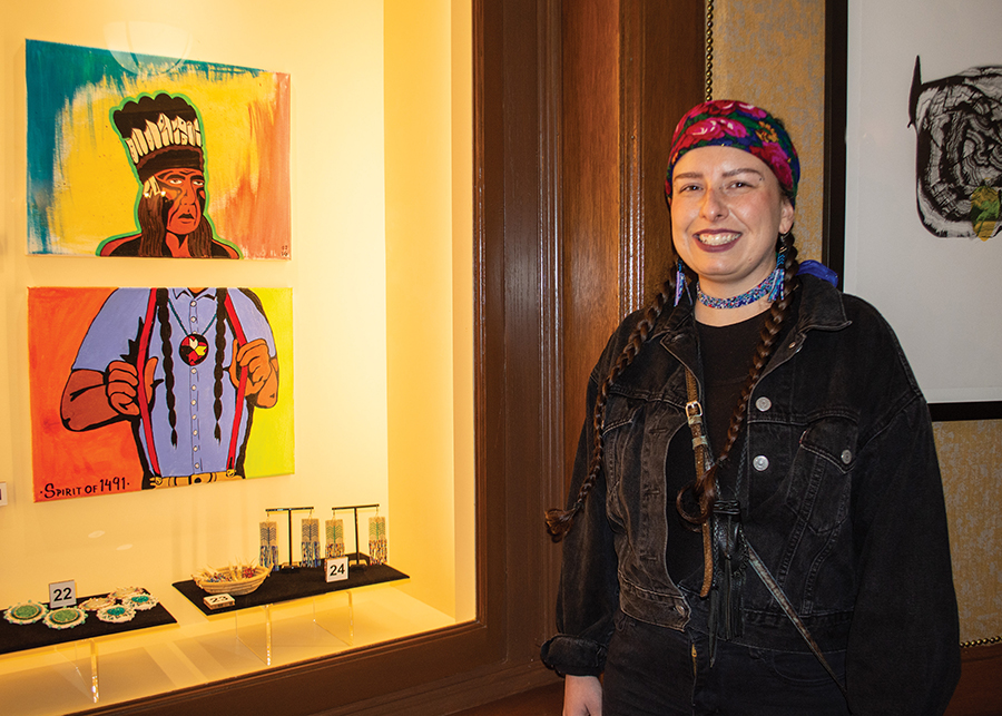 A person is smiling next to a table of her beadwork.