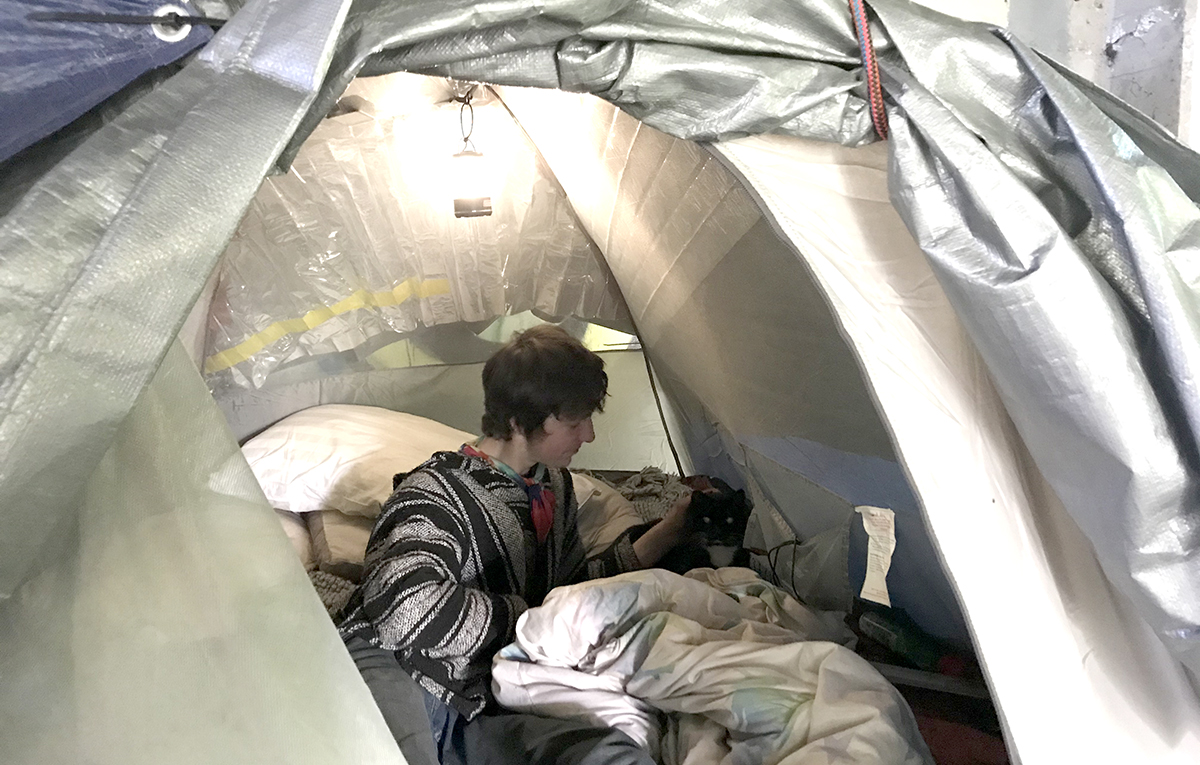 Austin reclines inside his tent and pets his cat