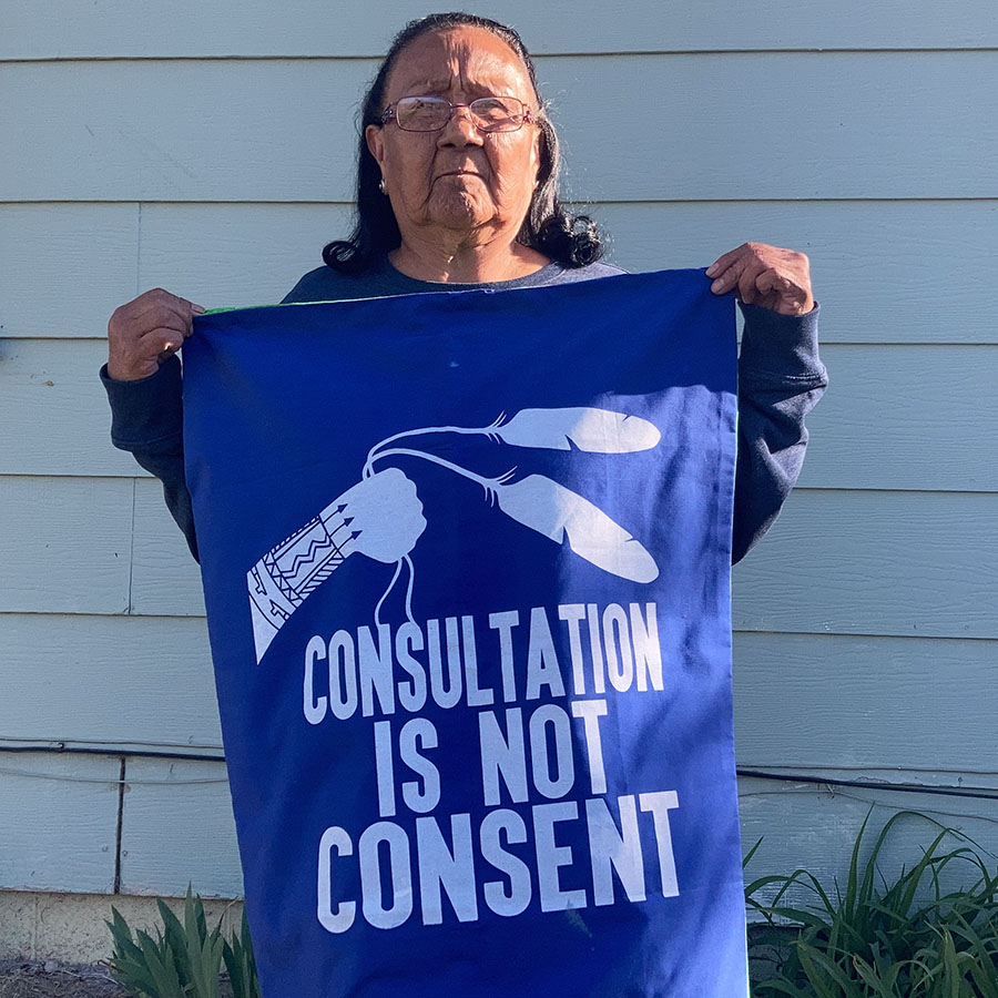 A person holds up a blue sign that says "consultation is not consent"
