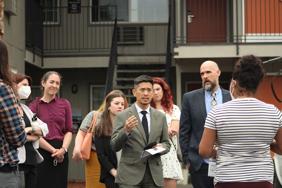 Richard Cho, wearing a suit, speaks to a crowd of people in a parking lot outside of the shelter. 