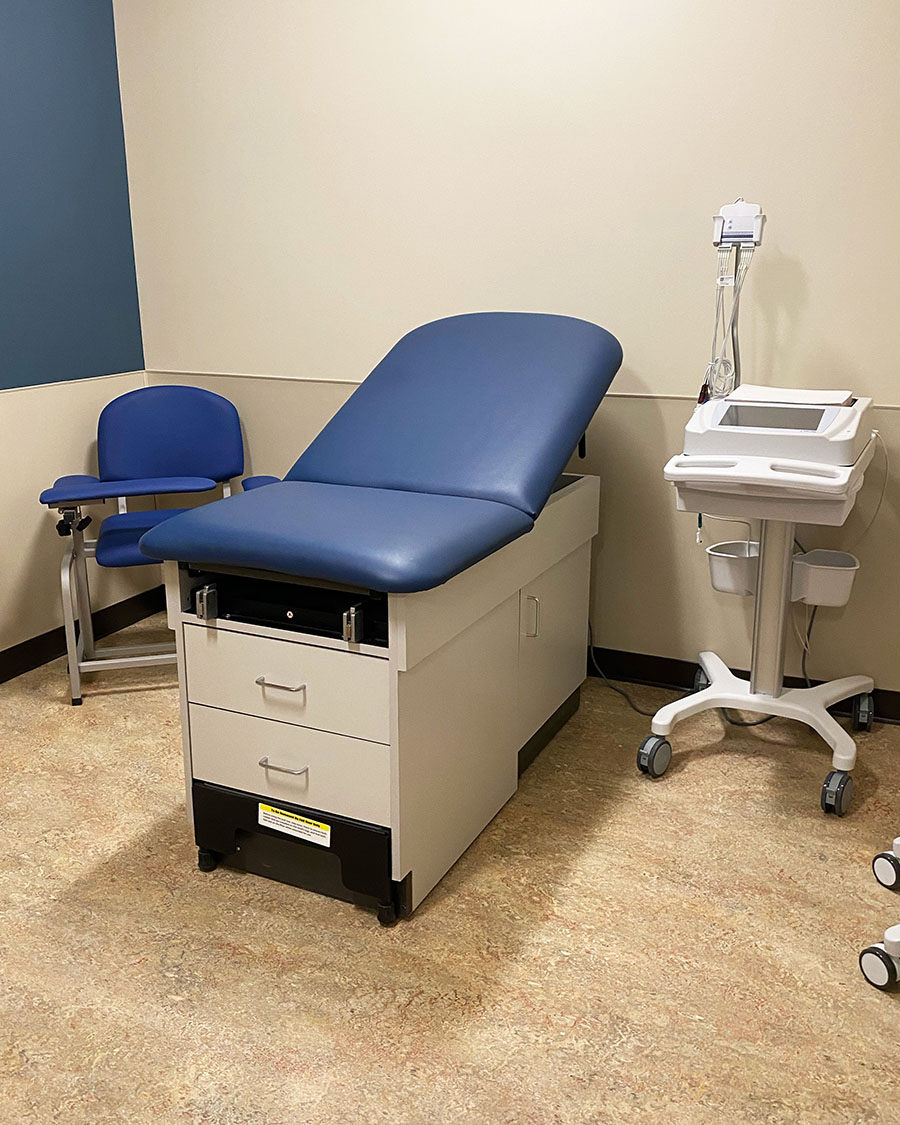 An exam room with an exam bed and chair in the corner.