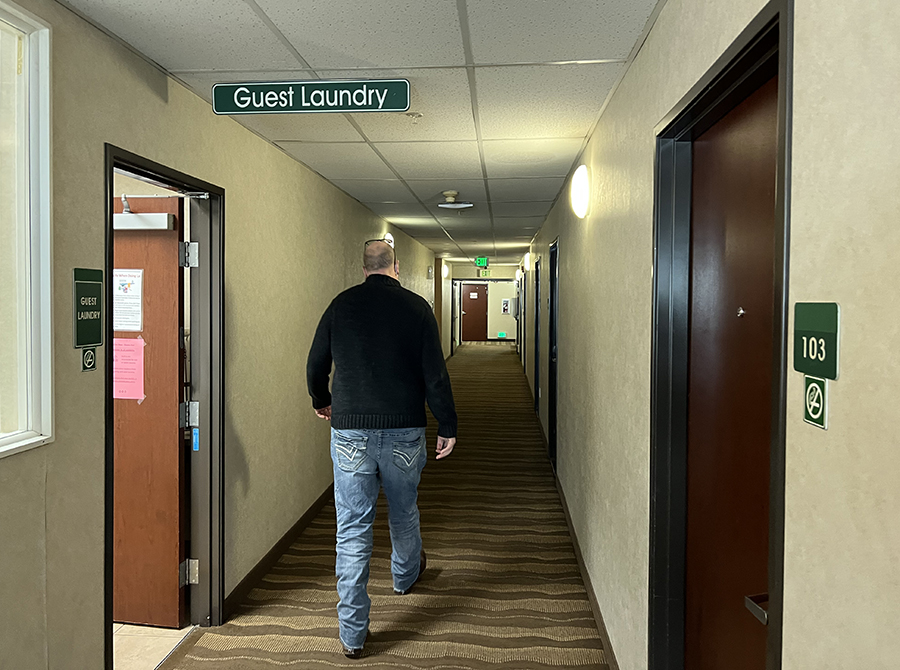 A man walks down a hallway with doors on either side and a sign that says "guest laundry" above him.