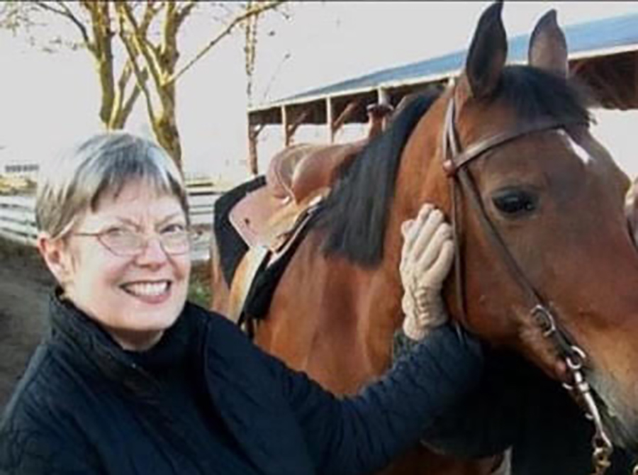 Sandra Lou Pollard smiles in a photo as she stands next to a horse with her hand resting on the horse's face.