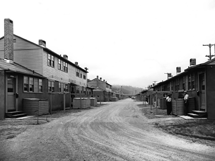 A black and white photo shows a dirt road lined with houses