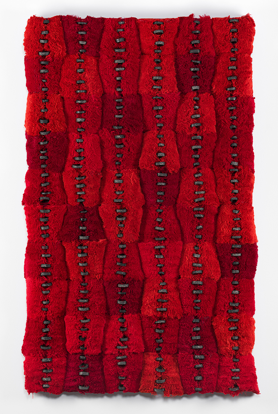 A red textured art piece hangs on a white wall.