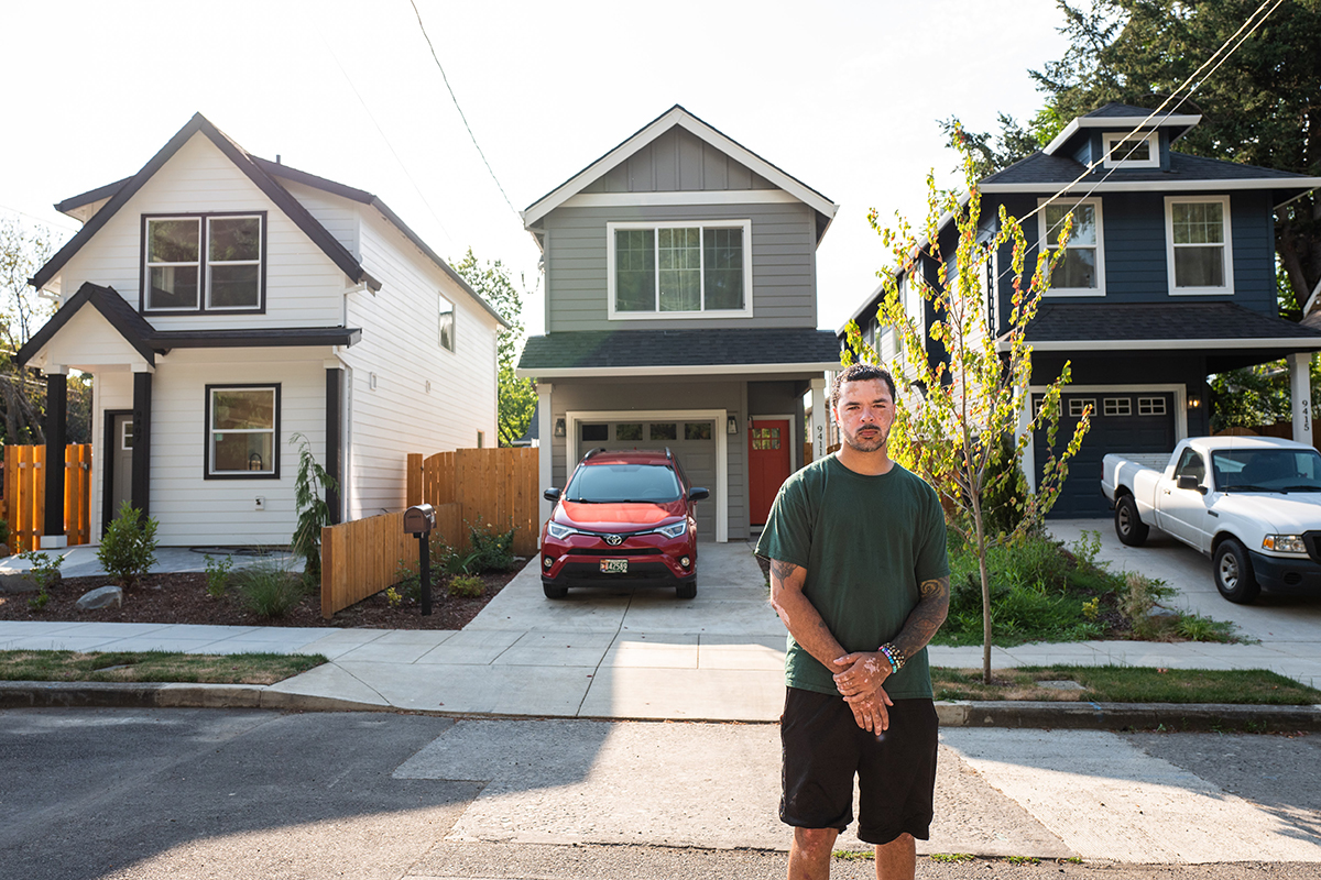 Mat Randol stands in the street in front of three houses that look nearly identical and newly built.