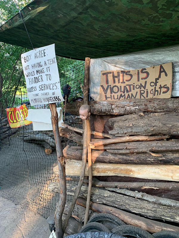 A sign that says "this is a violation of human rights"hangs outside a homeless encampment.