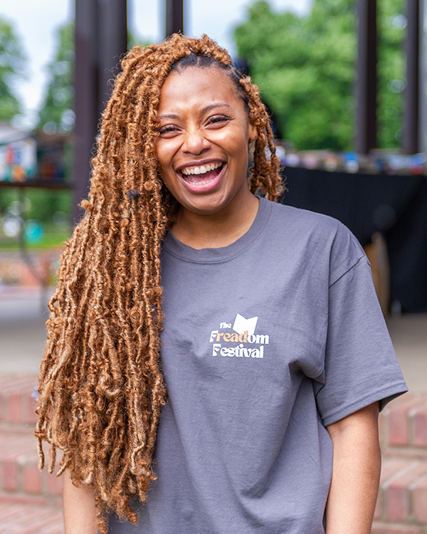 A portrait of Nanea Woods. She is wearing a gray shirt that says "Freadom Festival" and she is laughing.