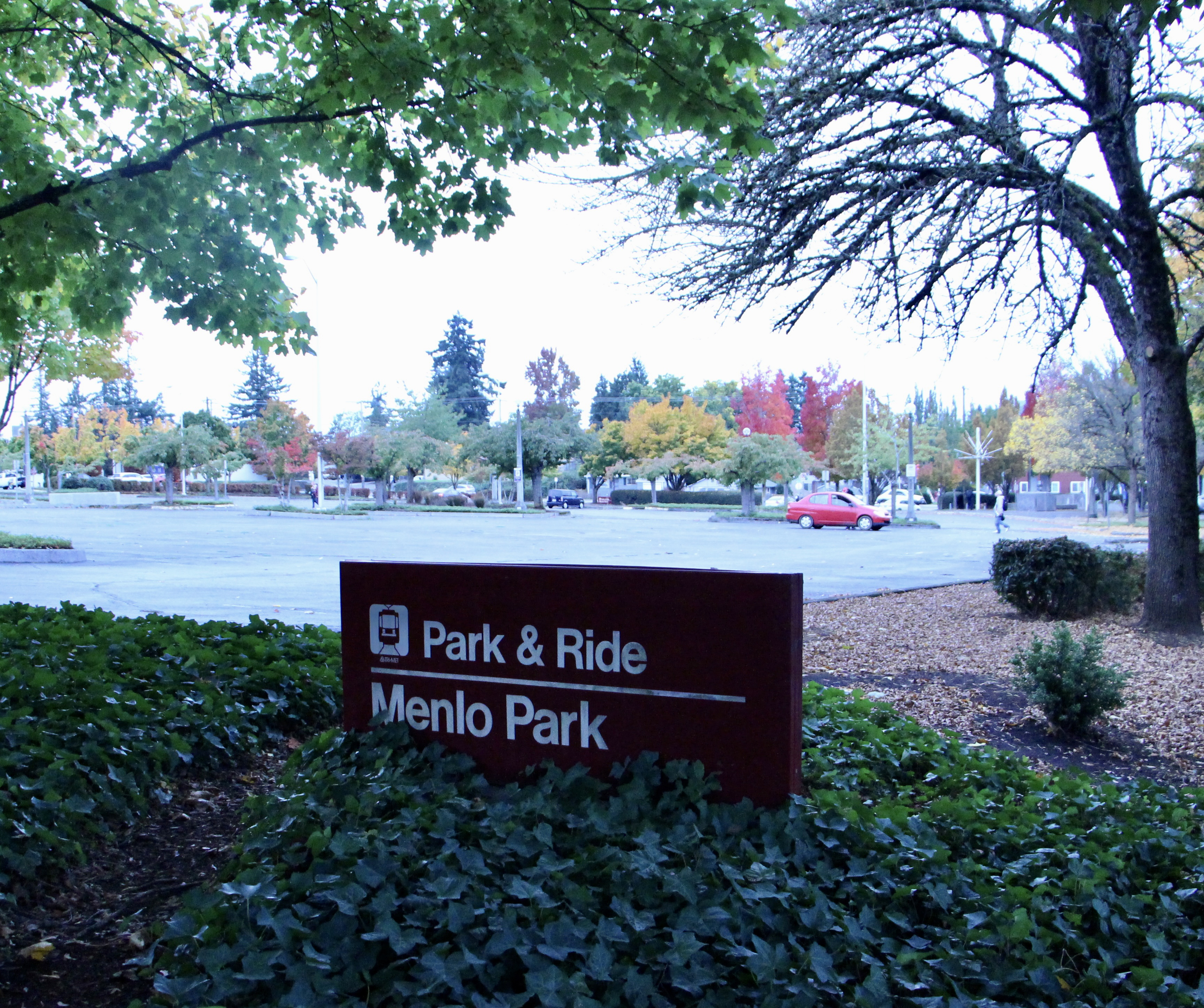 Photo of a sign in a patch of greenery in a parking lot. The sign says "Park & Ride Menlo Park."