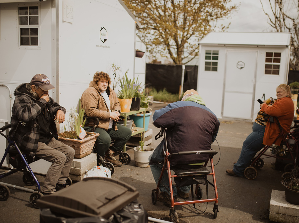 A group of people sits in a communal area outside of their mini-shelters in Salem.