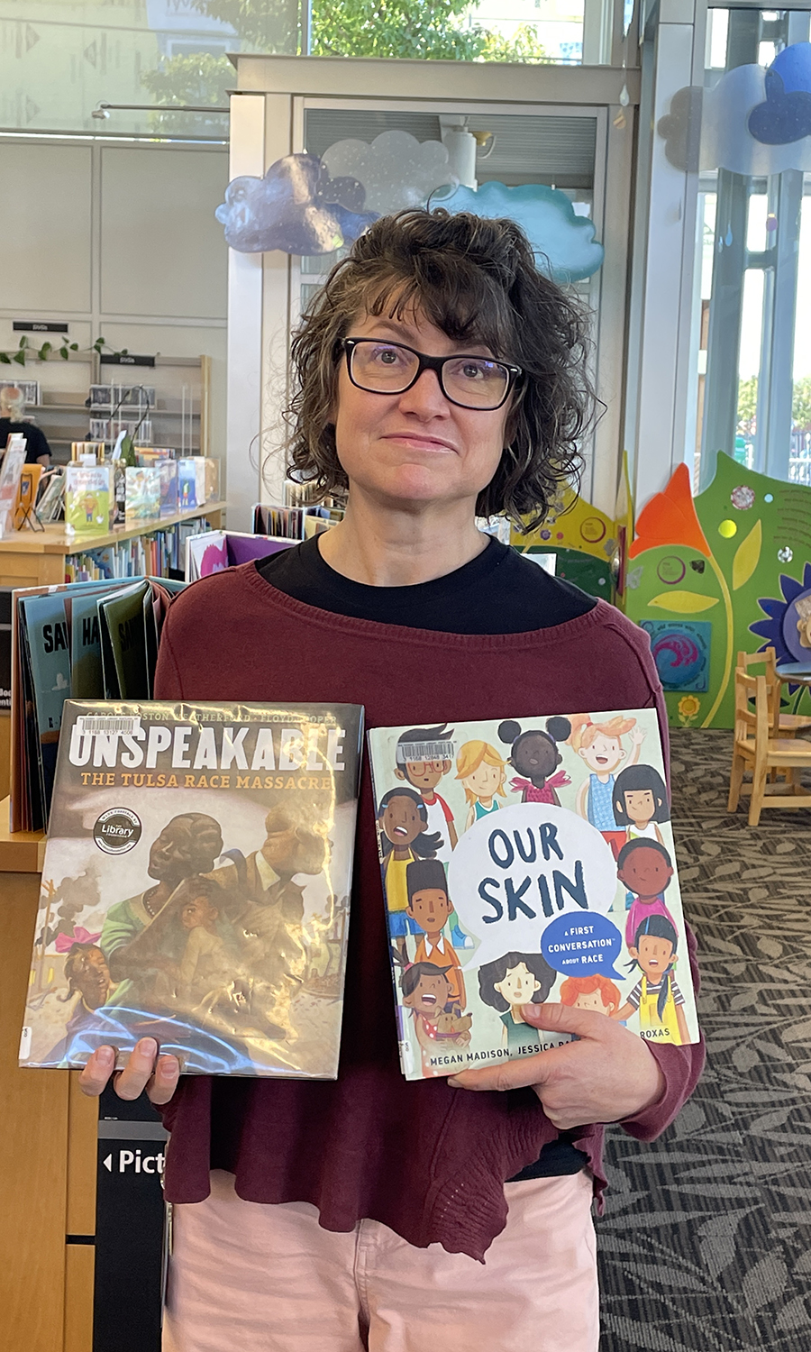 A librarian holds up the children's books "our skin" and "unspeakable" inside the Woodstock library.