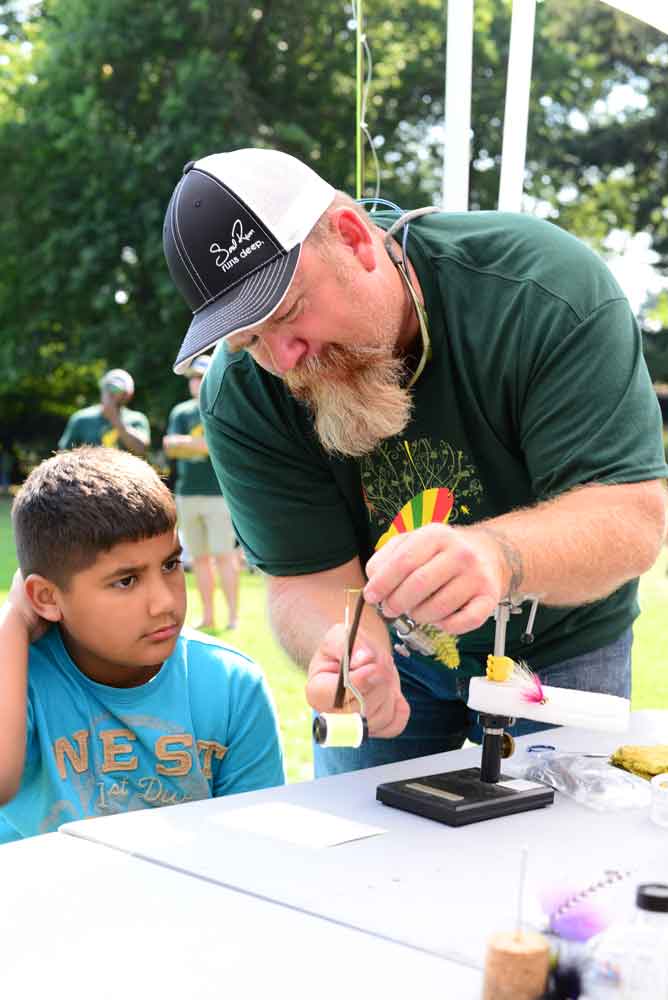 Army veteran Jason Small, a volunteer with Soul River Inc., shows a young man how to tie a fly for fishing.