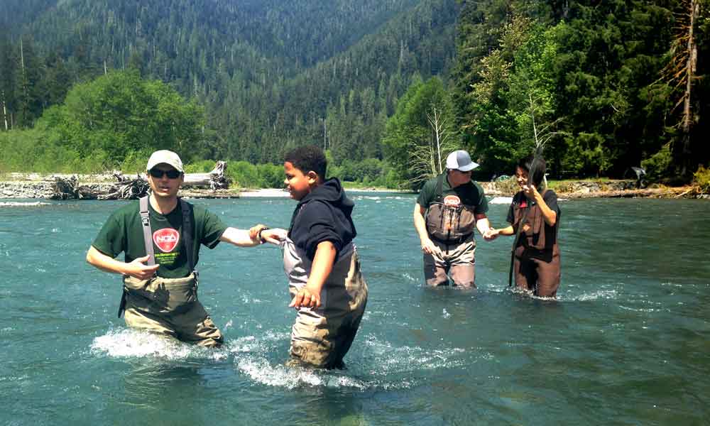 Army veteran John Hicks (far left) and Navy veteran Mark Roberts (second from right), guide youths into the Hoh River to practice wading.