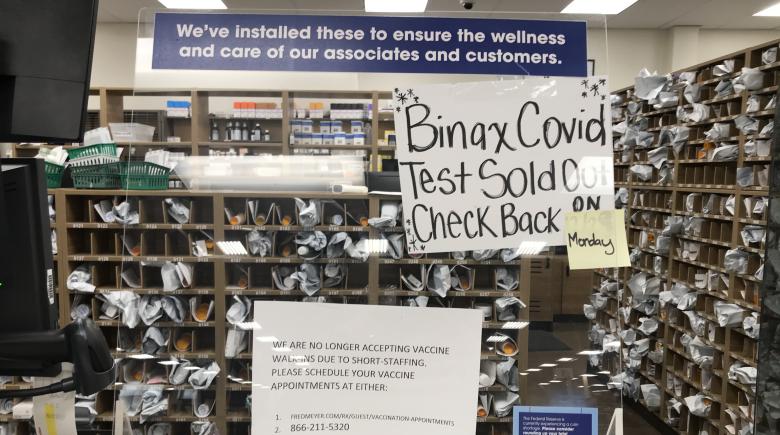 Photo of a pharmacy counter with signs indicating that COVID-19 tests are sold out and to check back on Monday. Another sign indicates they are not accepting walk in vaccine visits and one should schedule an appt. online.