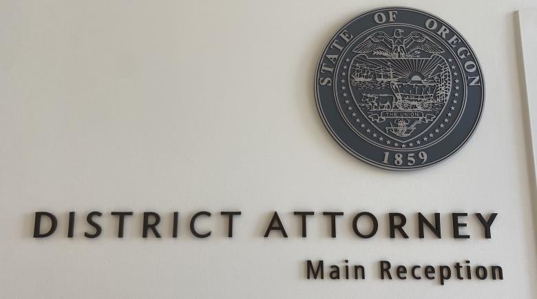 A white wall with words on it says, "District Attorney. Main Reception." To the right of the text is the State of Oregon Seal.