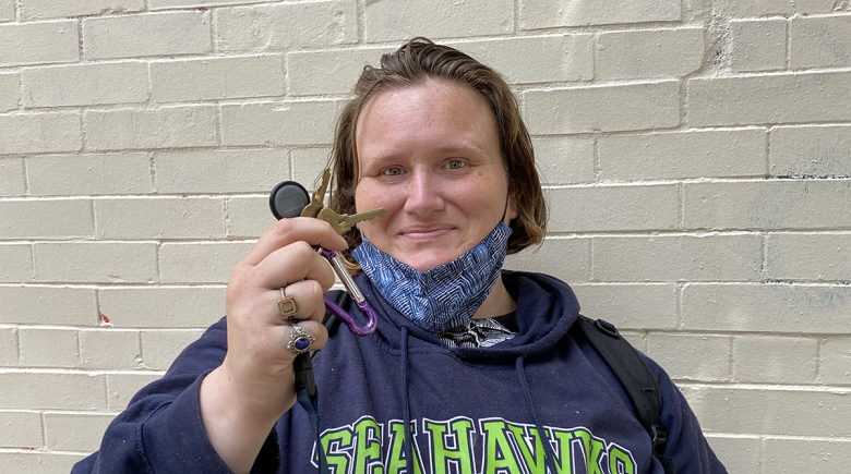 Wearing a blue Seattle Seahawks hoodie, Elizabeth smiles for a photo holding up a set of keys on a key ring in her hands.