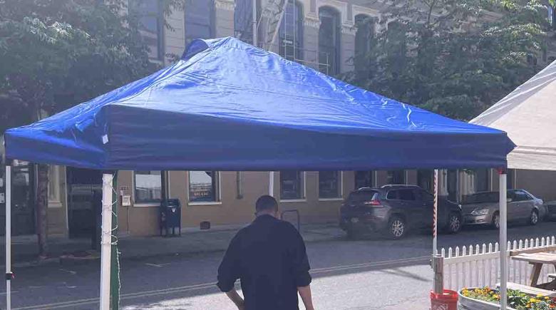A person stands under a blue outdoor canopy tent to get misted outside of Street Roots office.