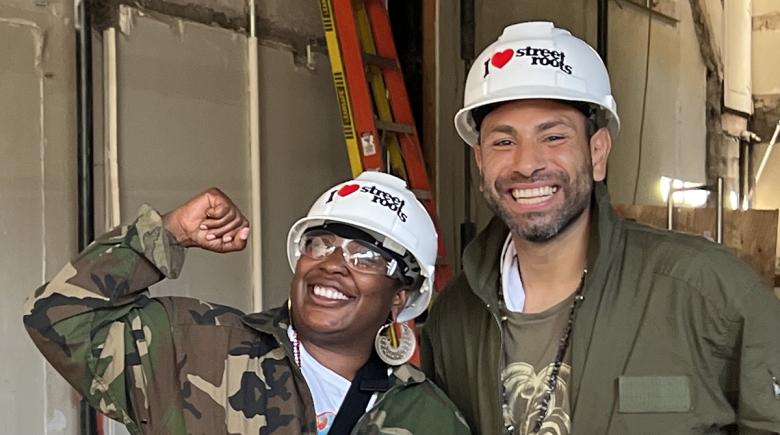 Laquida Landford and Christopher Murillo smile for a photo wearing white hard hats at a construction site.