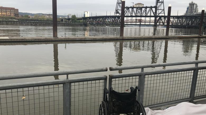 A wheelchair sits behind the fence that faces the Willamette River along the Eastbank Esplanade.
