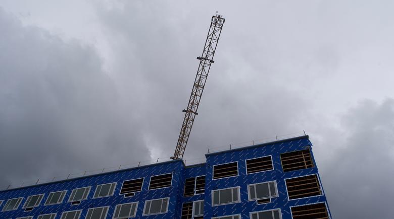 A tower crane hovers above a new housing development in downtown Portland. The sky is cloudy and gray.