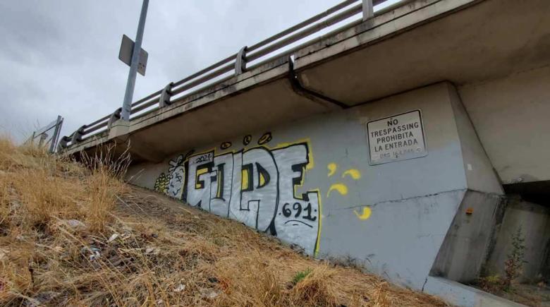 White, black and yellow graffiti underneath a freeway overpass. 