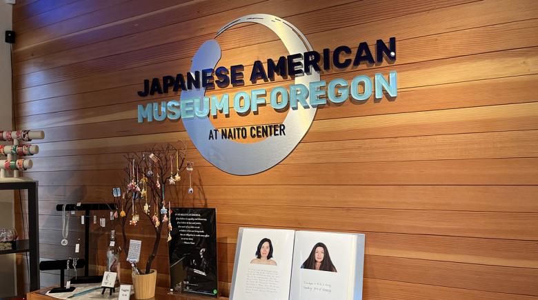 The logo of the Japanese American Museum of Oregon in the entryway of the museum sits above a table with a photo from the hapa.me exhibit.