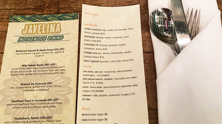 The Javelina menu next to a drink menu and silverware folded into a cloth napkin.
