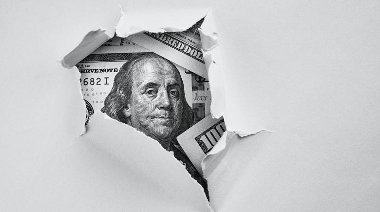 A tear in paper reveals Benjamin Franklin and hundred dollar bills.