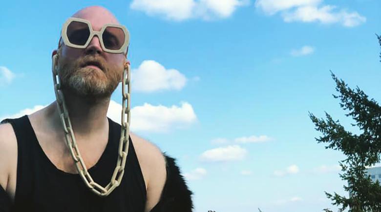 Logan Lynn is wearing a black tank top and is wearing large sunglasses with a large chain.
