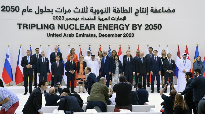 World leaders stand in front of rows of flags and pose for a photo. Words on the wall above them say, "Tripling Nuclear Energy by 2050."