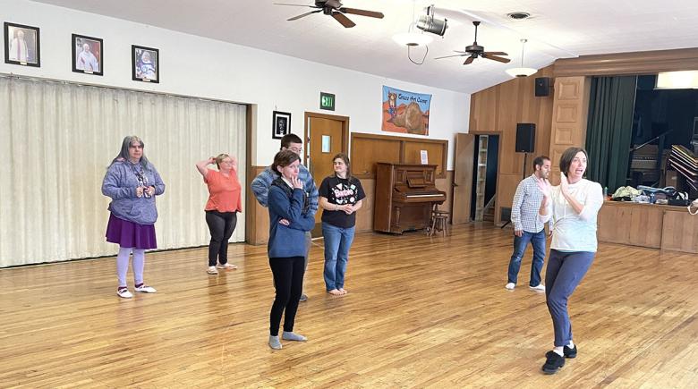 A group of students attends ballet class while an instructor leads them.