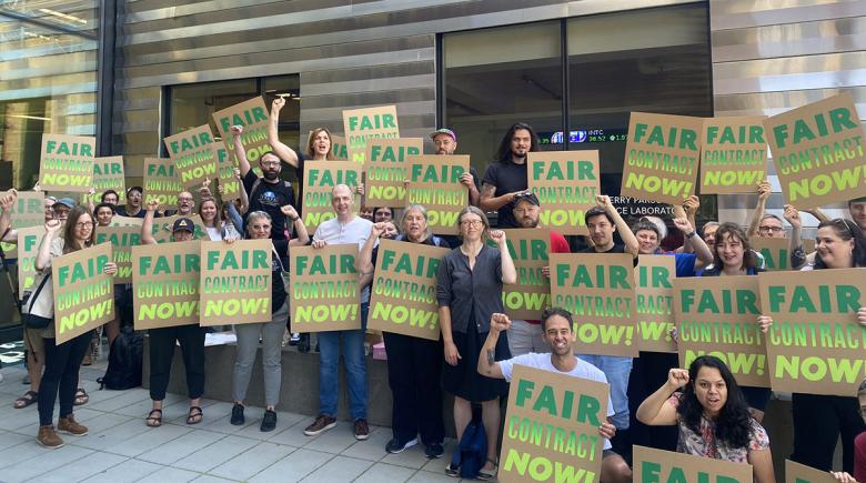 A group of people holding signs that say "fair contract now," pose for a photo.
