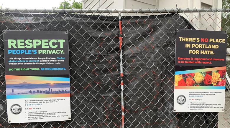 Two signs hang on a fence outside the Queer Affinity Village. The signs say, "respect people's privacy" and "there's no place in portland for hate"