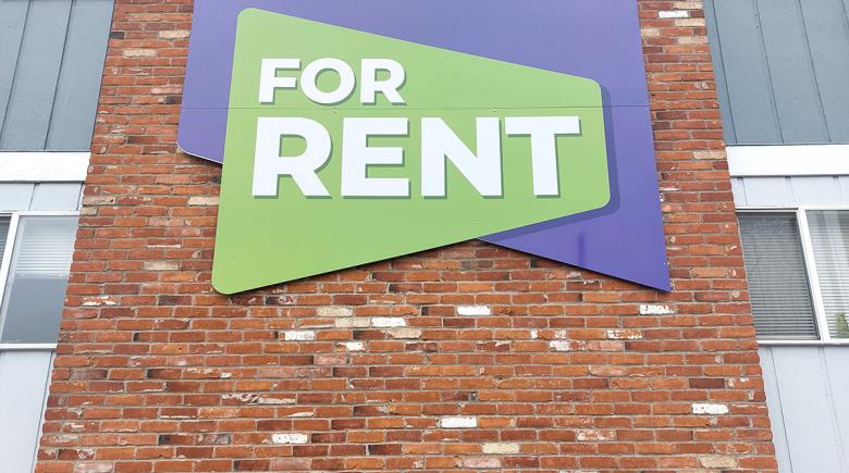 A photo of a "for rent" sign on a brick wall of a building