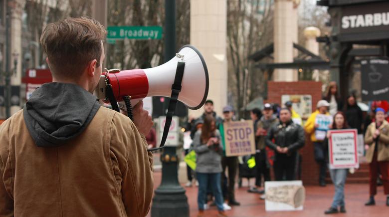 A person speaks into a megaphone addressing a crowd.