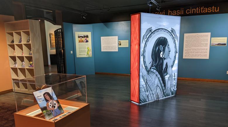 A view of the exhibit at the Chachalu Cultural Museum. There is a large portrait to the right and a children's book in a case in the foreground.