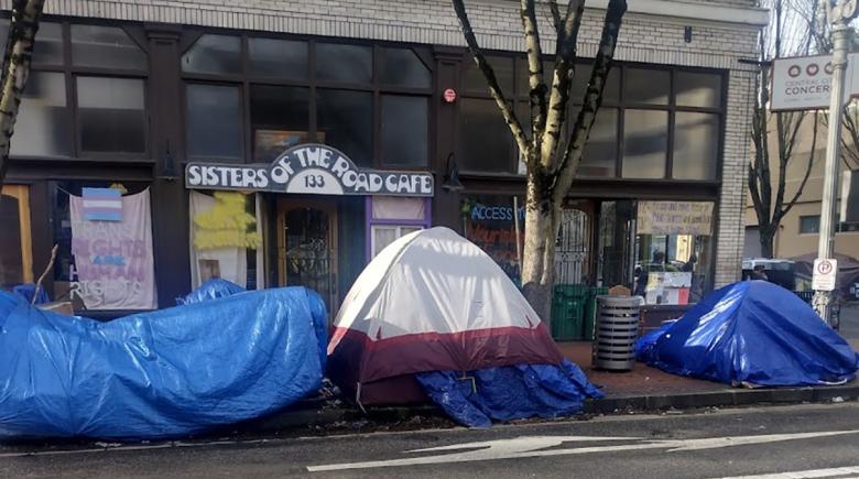 A photo outside Sisters of the Road Cafe with tents on the sidewalk in front of it.