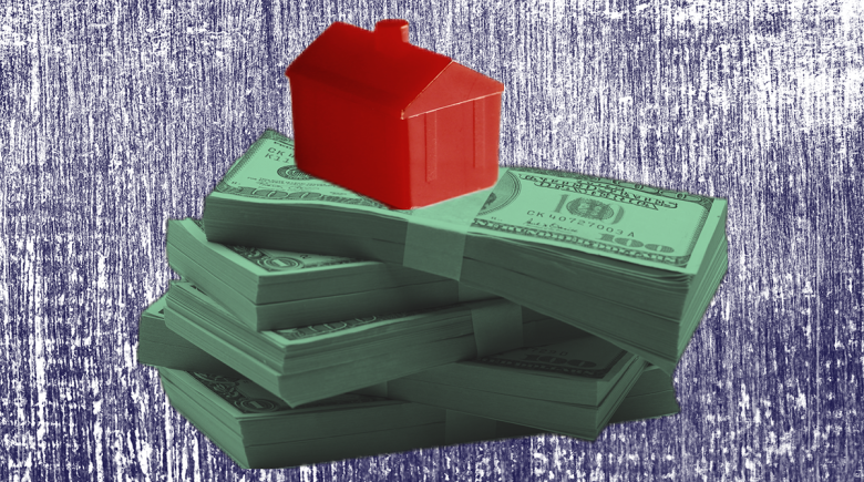 A stack of money sits in the center of the image with a tiny red plastic house sitting atop the pile of money.