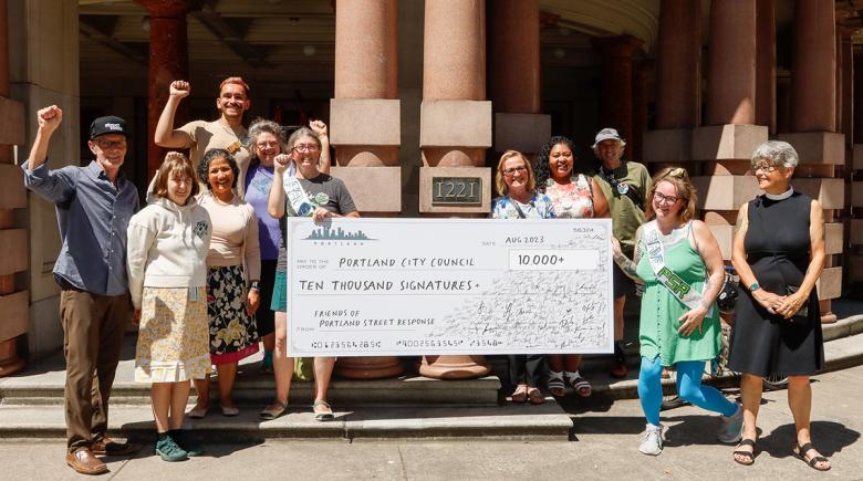 A group of 12 people stands outside Portland City Hall holding up a giant check showing the amount of signatures on the petition.