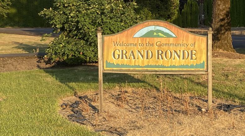 A wooden sign says "Welcome to the community of Grand Ronde"