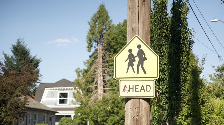 A photo of a yellow "pedestrian crossing" sign which shows two black silhouettes of figures walking across a street.