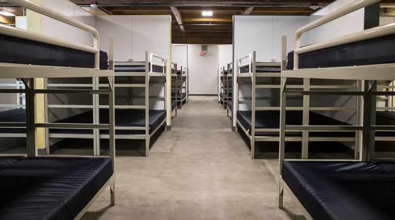Rows of bunk beds line both sides of a room in a shelter. 