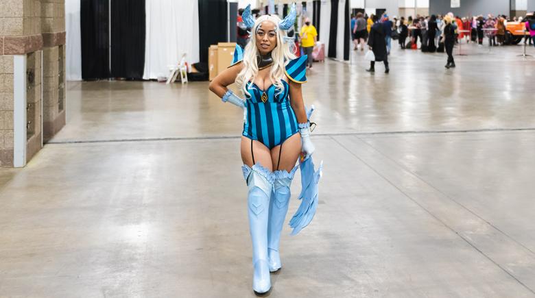 A photo of cosplayer Tif Von Batsy posing. She is wearing a blue striped bodysuit and has accessories for her cosplay costume.